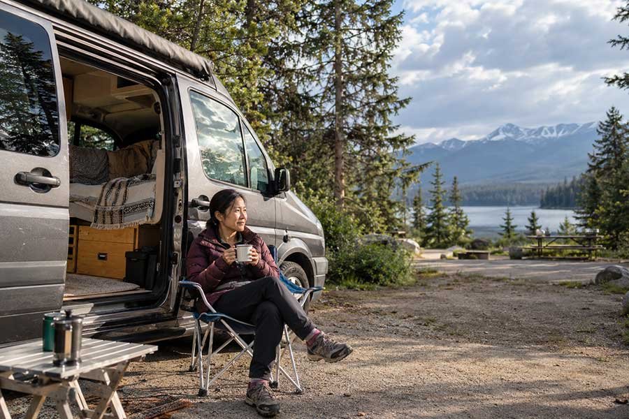 Beginner camper enjoying a quiet morning beside a campervan with a warm drink