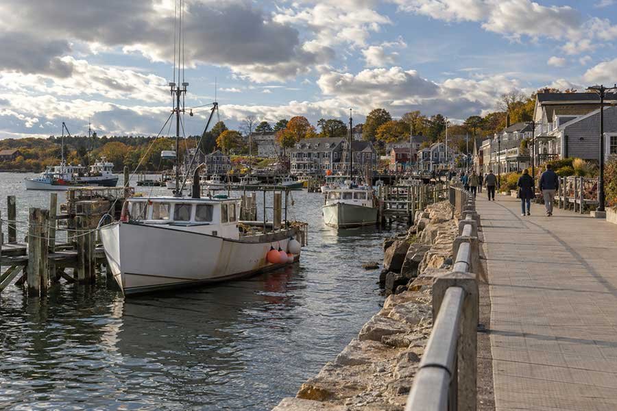 Travelers strolling along a working harbor in autumn with fishing boats and warm light