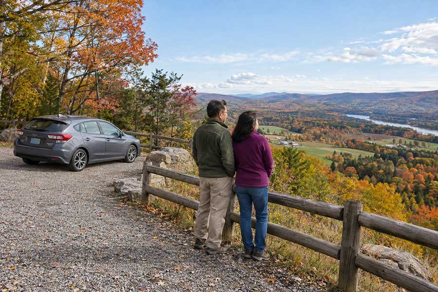 Travelers pausing at an autumn overlook on a scenic drive with colorful hills in the distance
