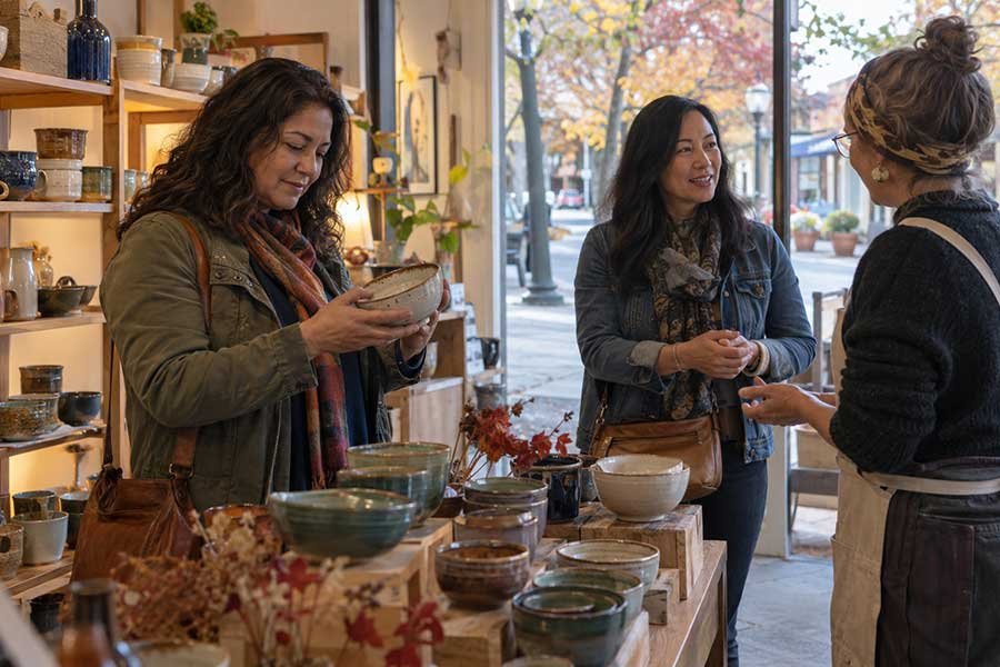 Friends browsing handmade pottery in a small shop during a fall festival weekend