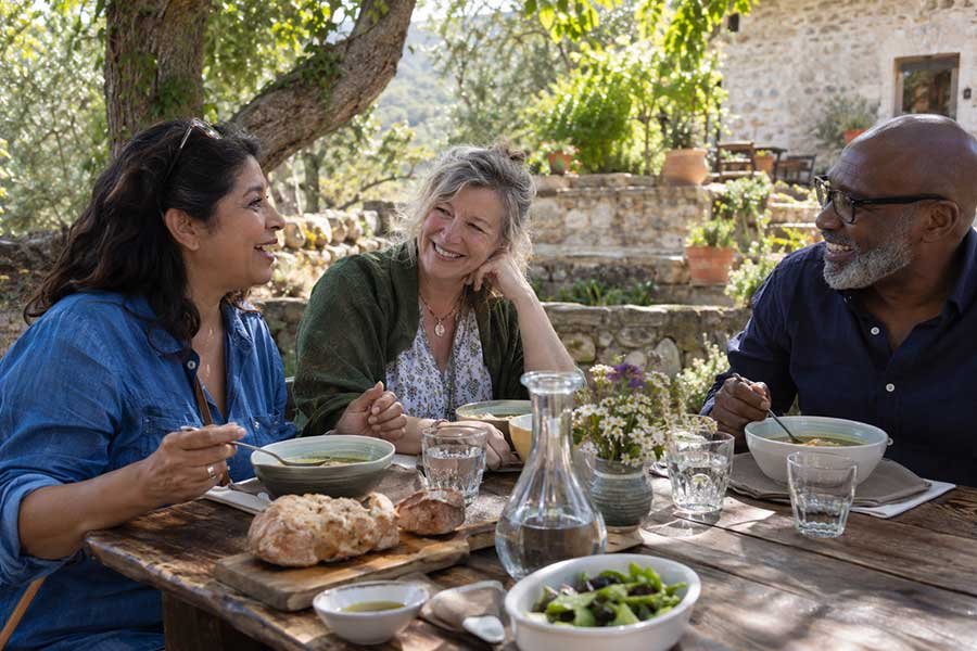 Friends laughing together over a candid countryside lunch at a long outdoor table