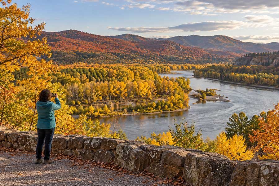 Travelers chasing autumn colors along a quiet river trail on a fall road trip
