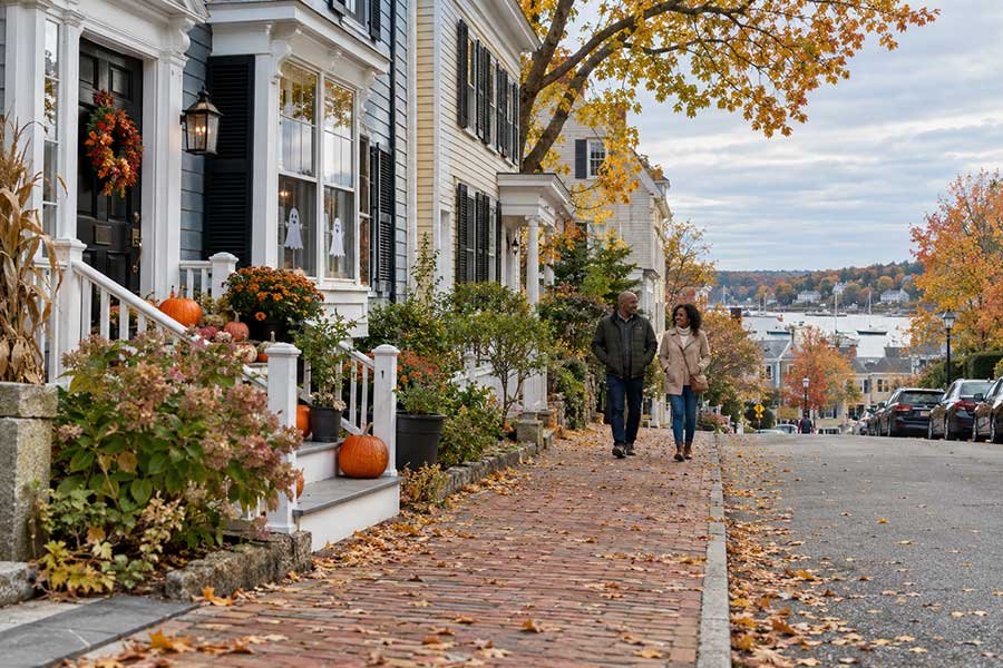 Couple on a coastal autumn stroll past pumpkins and gentle Halloween decorations in a harbor town
