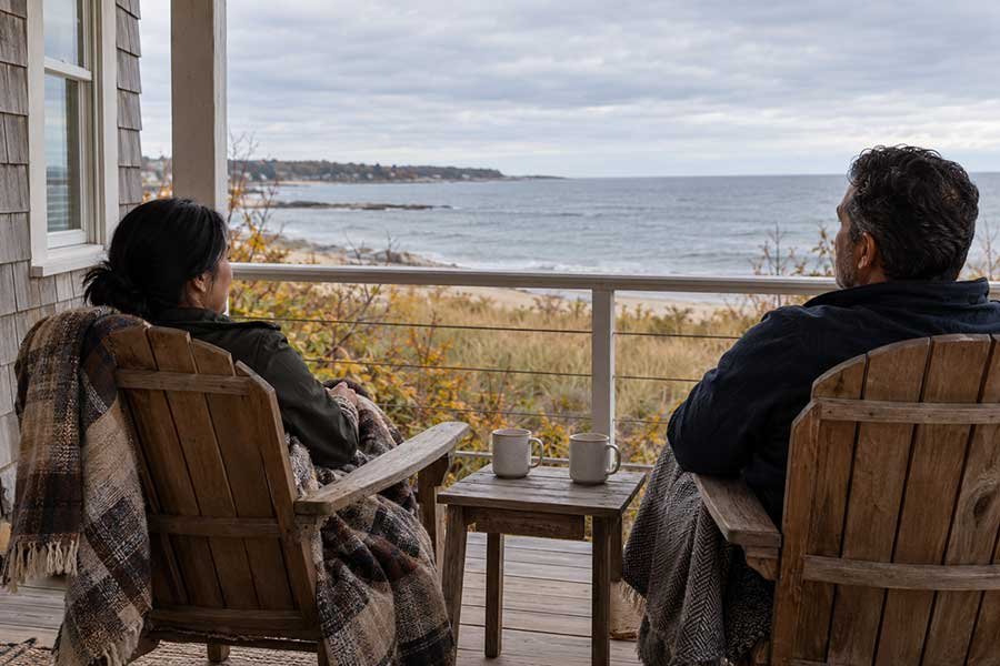 Couple enjoying a cozy fall seaside getaway with a blanket, warm drinks, and a view of the water