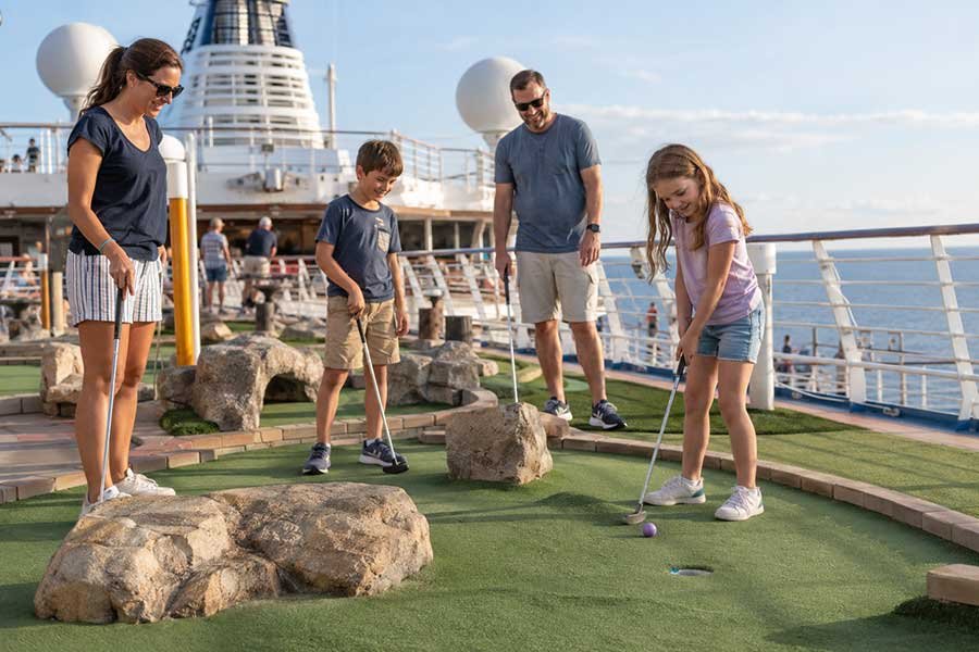 Family playing mini golf on the upper deck of a cruise ship with the sea behind them