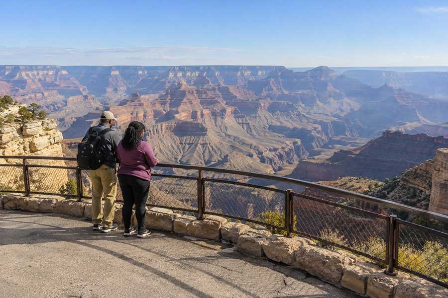 Visitors at a Grand Canyon South Rim overlook looking out over layered red rock cliffs