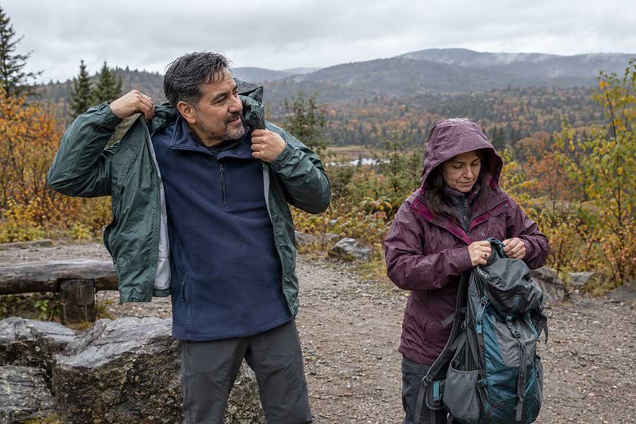 Hiker putting on a rain jacket and pack cover before a rainy fall hike